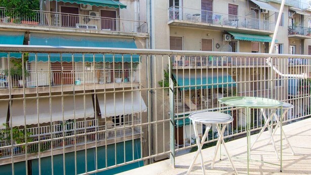A multi-story residential building with balconies, a gated entrance, and a small outdoor seating area with tables. - Sunny 1bd Apartment Just 1minute to Acropolis (Athens)