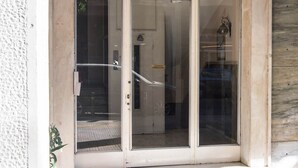 A building entrance with a glass door, a number '15' above it, and a small plant to the left. - Sunny 1bd Apartment Just 1minute to Acropolis (Athens)