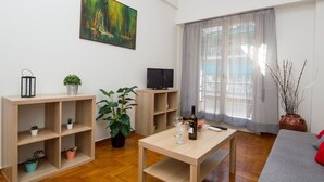 A modern living room with a wooden floor, a TV, a table with a bottle and glasses, and potted plants. - Sunny 1bd Apartment Just 1minute to Acropolis (Athens)