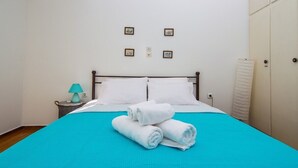 A neatly made bed with a blue bedspread and white pillows, a teal lamp on a bedside table, and a white towel rolled up on the bed. - Sunny 1bd Apartment Just 1minute to Acropolis (Athens)