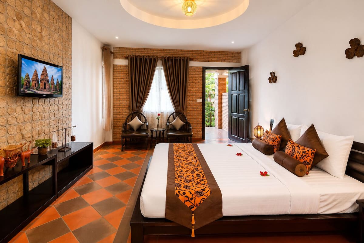 Une chambre d’hôtel avec un grand lit, un téléviseur fixé au mur, un mur en briques et une vue sur l’extérieur.