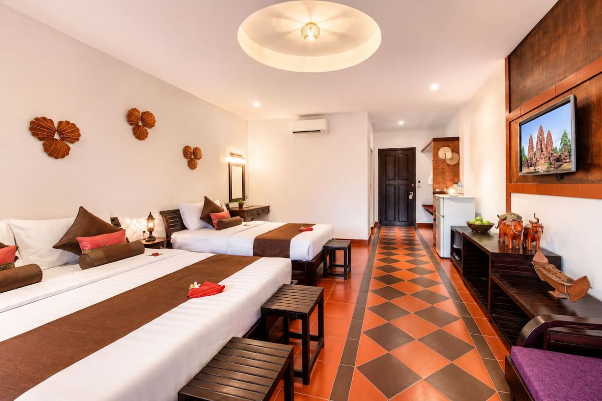 Une chambre d’hôtel avec deux lits, une petite kitchenette, une salle de bain et un coin repas avec un sol à carreaux.