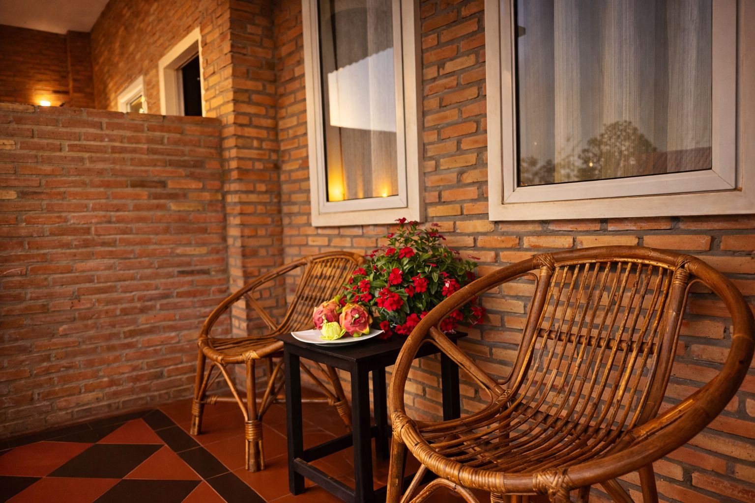 Pared de ladrillo con una ventana, una mesa con sillas y flores.