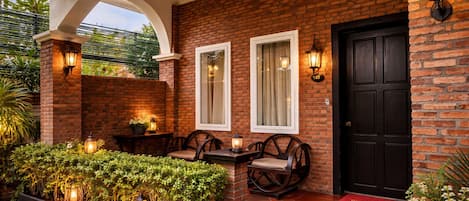 Fachada de ladrillo con puerta negra, dos ventanas y terraza con faroles.
