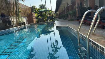 A swimming pool with clear blue water, surrounded by a brick building and palm trees.