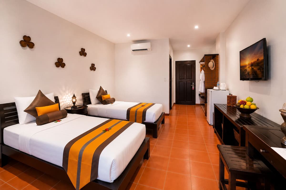 Une chambre d’hôtel avec deux lits, un bureau, une chaise, une télévision et une porte donnant sur une salle de bain.