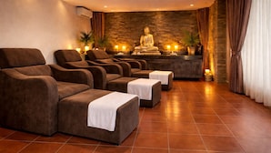 Ein Spa-Raum mit mehreren Massagesesseln, einer Buddha-Statue und einer Steinwand.