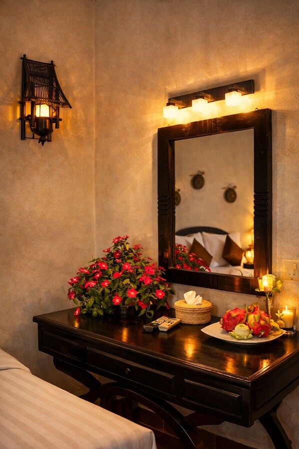 A hotel room with a wooden dresser, a mirror with lights, a vase of red flowers, a candle, and a remote control. - Kravan Siem Reap Boutique Villa (Siem Reap)