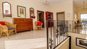 A spacious living area with a wooden dresser, wicker chairs, a chandelier, and a balcony with a wrought iron railing. - Ta Joseph (Xewkija)