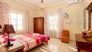 A bedroom with a bed, a wooden wardrobe, a chair, a desk, and an air conditioning unit. - Ta Joseph (Xewkija)