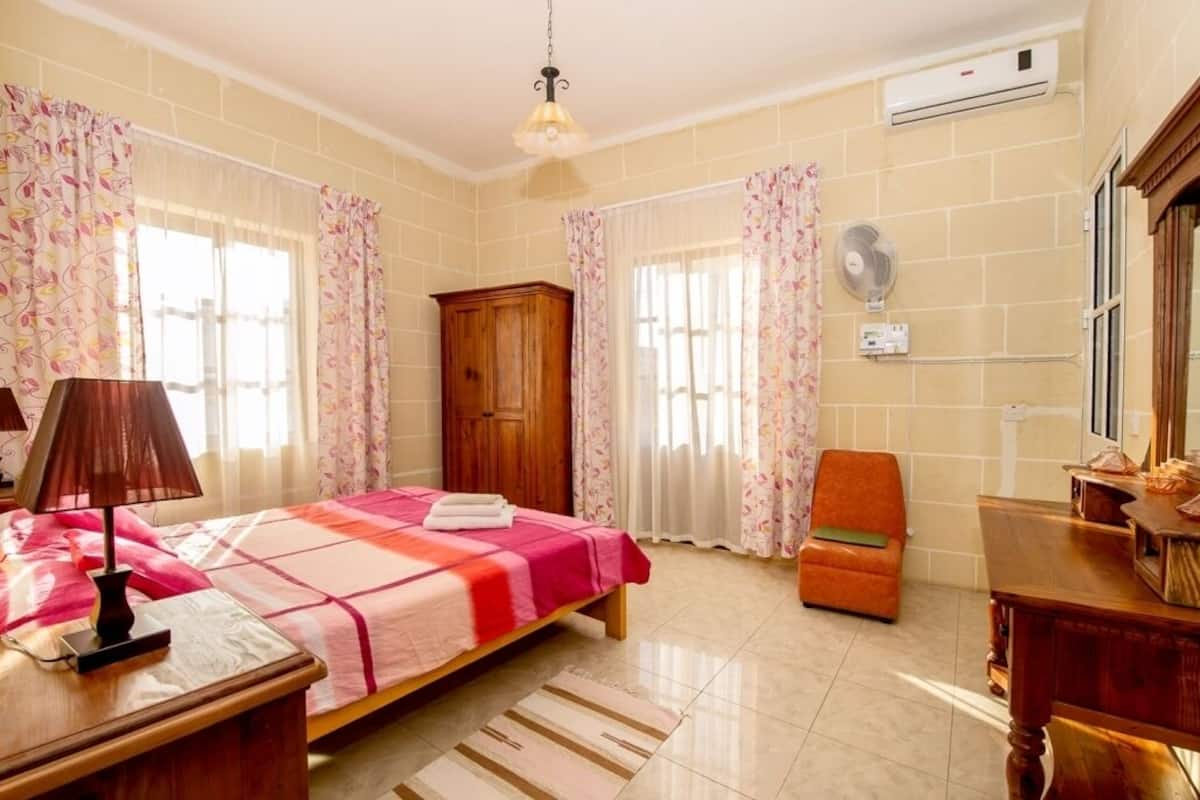 Une chambre à coucher comprenant un lit, une armoire en bois, une chaise, un bureau et un appareil de climatisation.