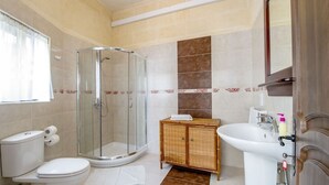 A bathroom with a glass-enclosed shower, a toilet, a sink, and a cabinet. - Ta Joseph (Xewkija)