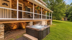 Ein Steinhaus mit einer Veranda, einem Whirlpool und einem Rasenstück.