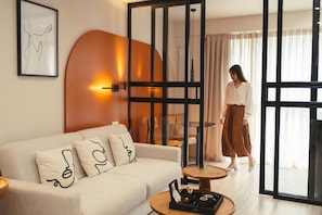 A modern hotel room with a white sofa, abstract pillows, a small round table with a tray, and a large window with curtains. - Finders Ermou Suites (Athens)