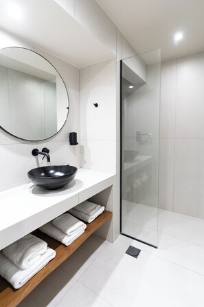 A modern bathroom with a round mirror, black sink, and glass shower enclosure. - Finders Ermou Suites (Athens)