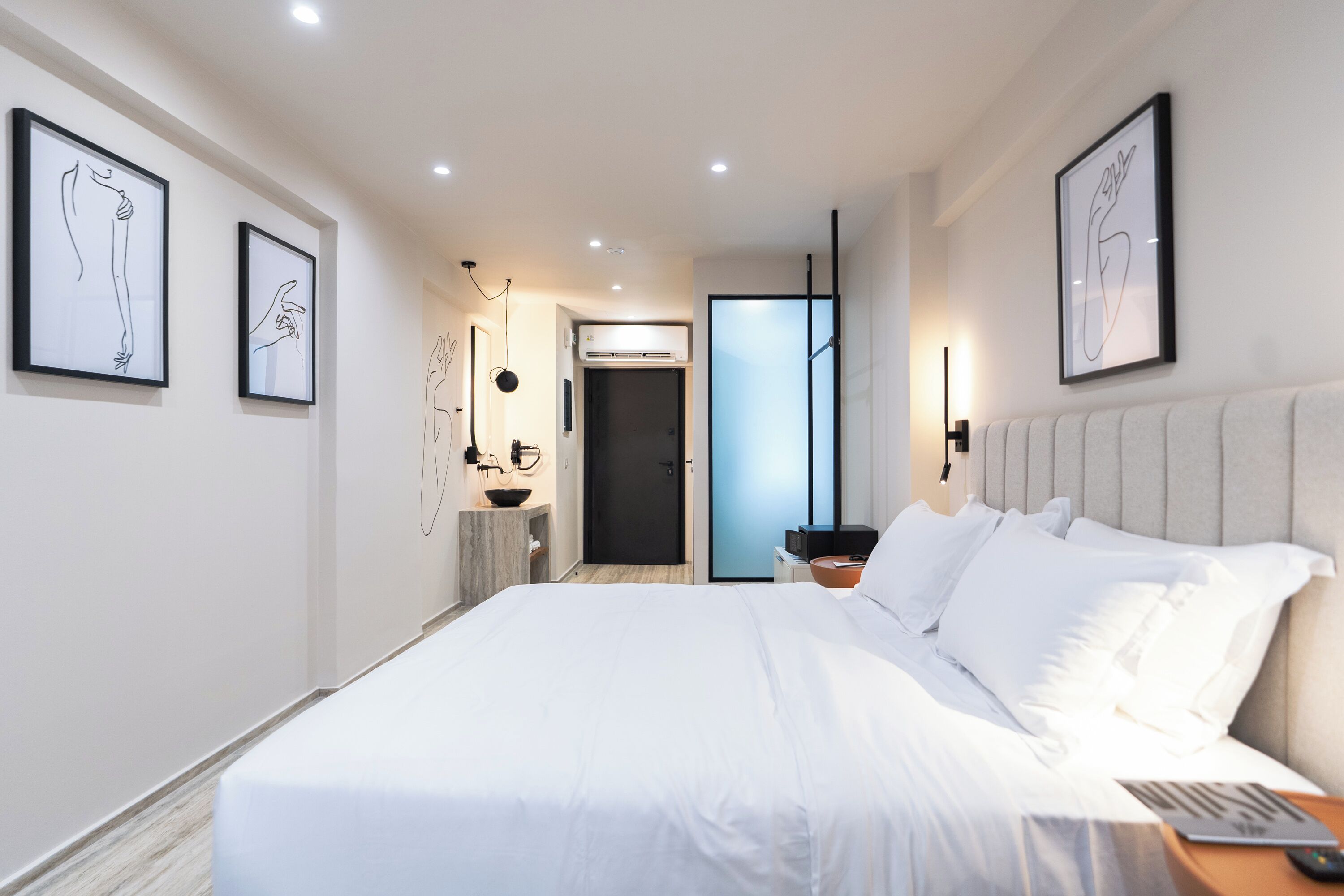 A modern hotel room with a large bed, framed artwork on the walls, a bedside table, and a door leading to another room.