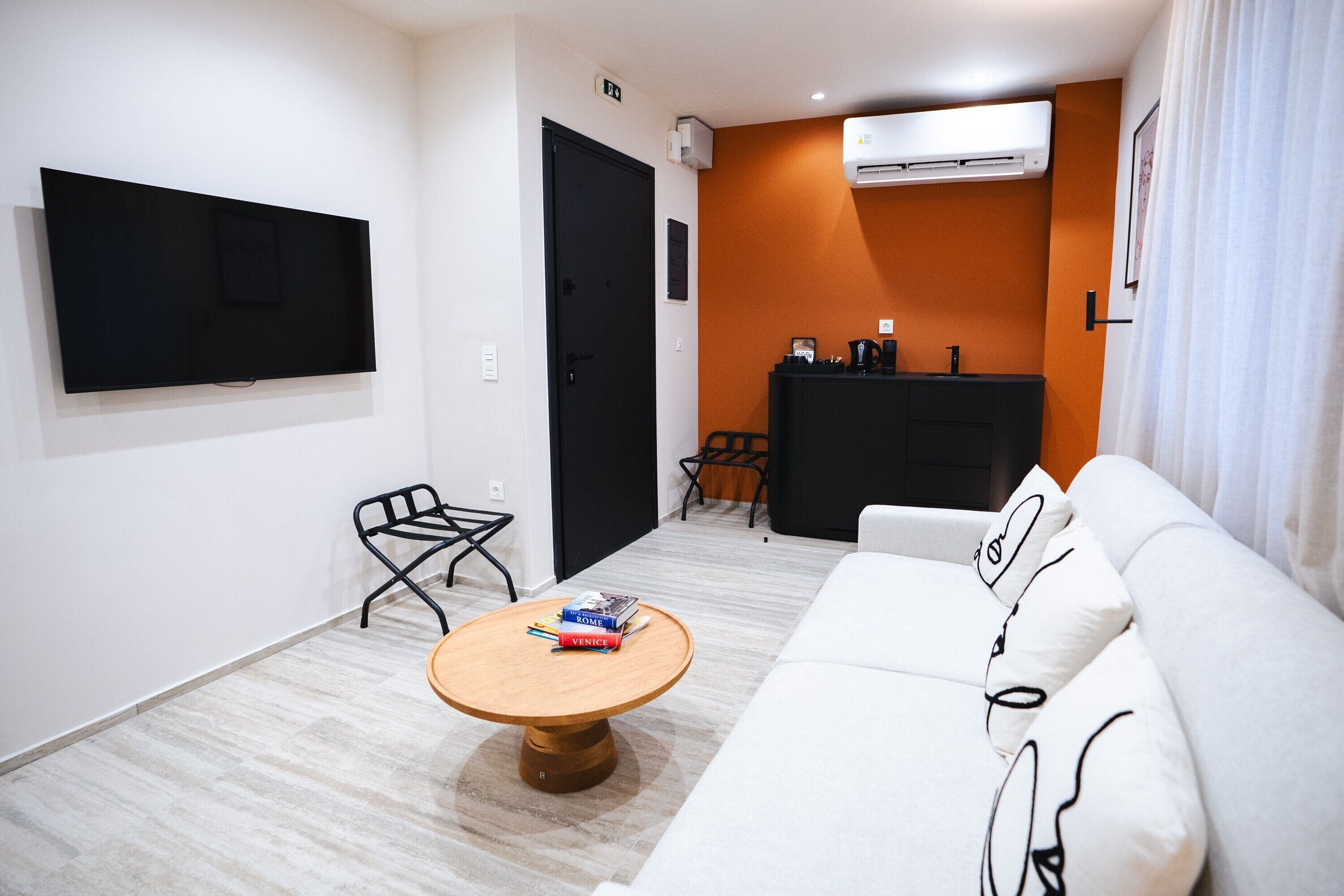 Uma sala de estar moderna com televisão de tela plana, um sofá, uma mesa de centro e um pequeno espaço de jantar com um armário preto e cadeiras.