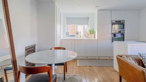 A modern kitchen with white cabinetry, a built-in oven, and a window with a view of the outside. - Chic 1BDR City Retreat with Views of the Shard (Greater London)