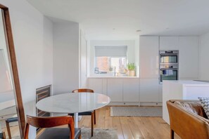 A modern kitchen with white cabinetry, a built-in oven, and a window with a view of the outside. - Chic 1BDR City Retreat with Views of the Shard (Greater London)