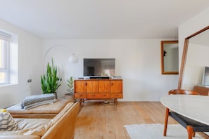 A modern living room with a wooden cabinet, a flat-screen TV, a dining table, and a large mirror. - Chic 1BDR City Retreat with Views of the Shard (Greater London)