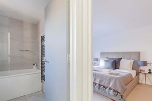 A modern bedroom with a large bed, a bedside table with a lamp, and a glass shower enclosure. - Chic 1BDR City Retreat with Views of the Shard (Greater London)