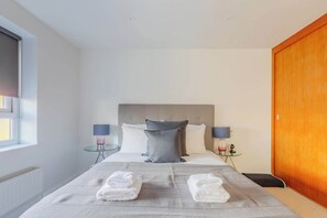 A hotel room with a bed, two bedside lamps, a wooden door, and a window. - Chic 1BDR City Retreat with Views of the Shard (Greater London)