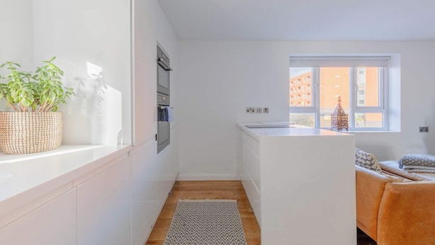 A modern kitchen with white cabinetry, a window, and a small island. - Chic 1BDR City Retreat with Views of the Shard (Greater London)