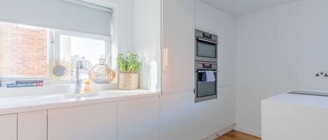 A kitchen with white cabinets, a built-in oven, a window with a view of a brick building, and a small rug on the floor.