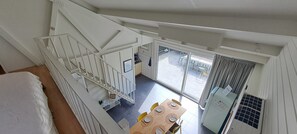 A high-ceilinged room with a staircase, a dining area with a table and chairs, and a view through a glass door to an outdoor patio. - De Haerde 27, quiet vacation park near the North Sea beach (Ellemeet)