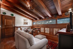 A cozy room with wooden beams, a sofa, a dining table, and a view through a window. - GuestHost - Charming 45 sqm apartment, with fine wooden finishes and mountain view, ideal for two guests, located on the 4th floor of a characteristic building. The property is located in the heart of Cortina, along the famous Corso Italia, a 7-minute wa (Cortina d'Ampezzo)