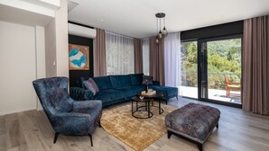 Un salon moderne avec un canapé bleu, un fauteuil à motifs et un pouf, une table basse et un tableau au mur.