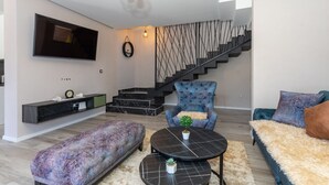 Un salon moderne avec un téléviseur à écran plat, un escalier et un fauteuil bleu.
