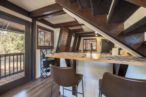 Ein Essbereich mit einem Holztisch und zwei Stühlen, einer Treppe und Blick auf Bäume durch große Fenster.