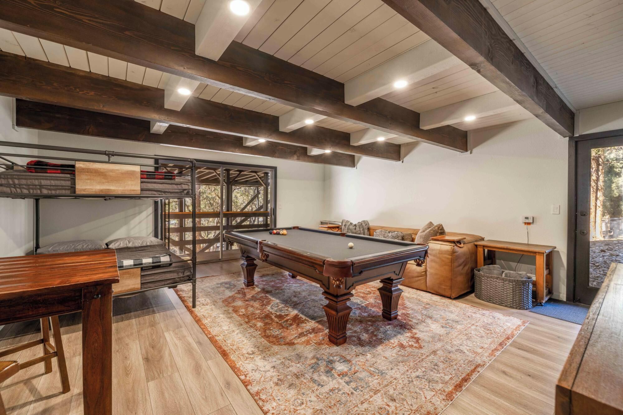 A pool table in a room with a wooden ceiling, a sofa, and a window.