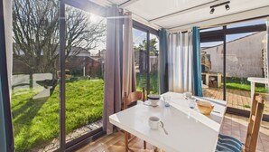 Un comedor moderno con una mesa blanca, sillas y vistas a un jardín verde a través de puertas de cristal amplias.