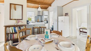 Un comedor acogedor con una mesa de madera dispuesta para cuatro personas, rodeado de estanterías y una cocina al fondo.