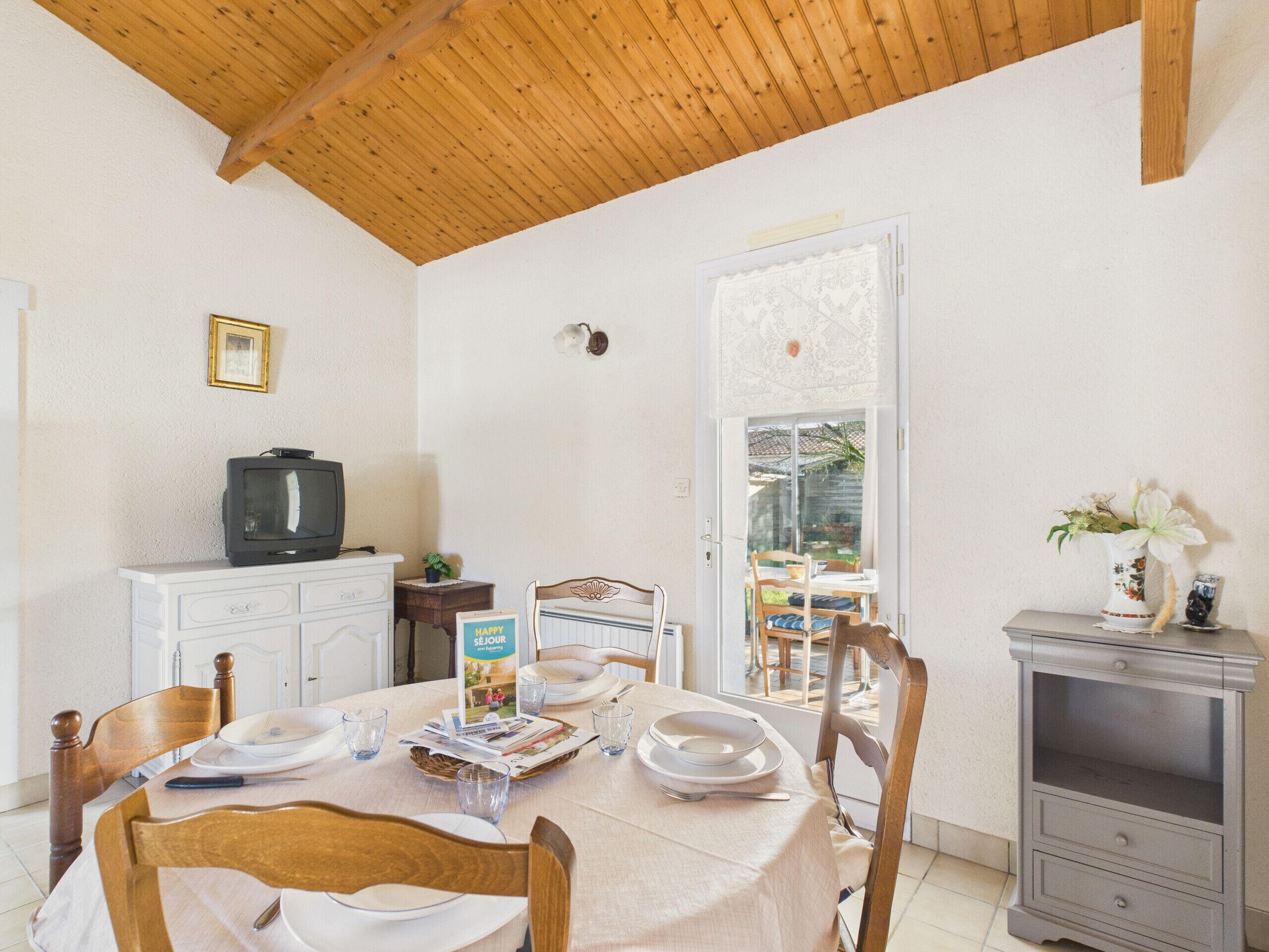 A dining area with a table set for four, a television on a cabinet, and a door leading outside.