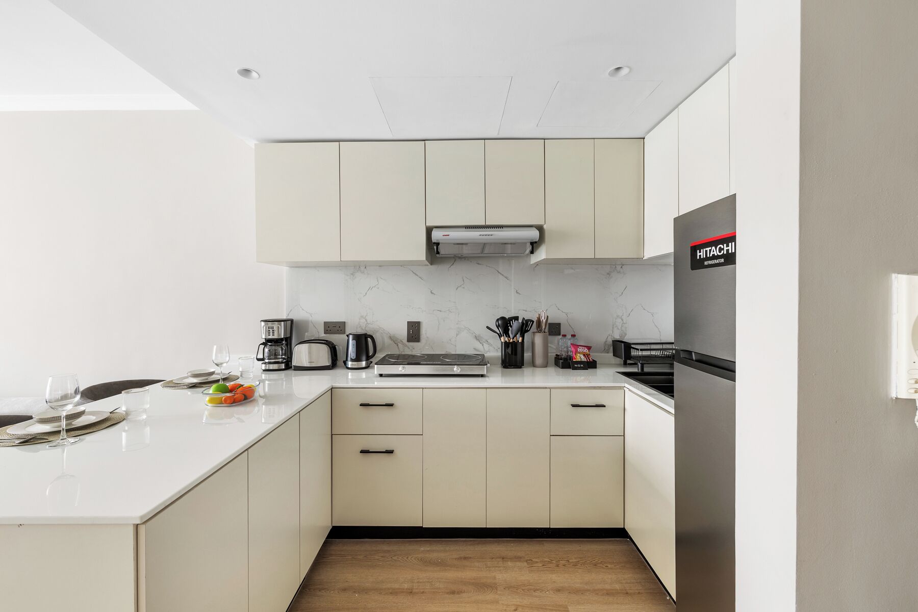 A modern kitchen with white cabinets, a built-in oven, a coffee maker, and a refrigerator.