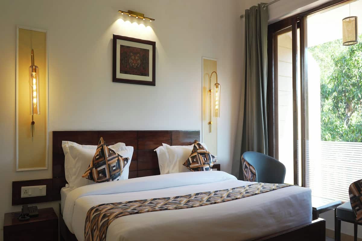 A hotel room with a large bed, two bedside lamps, a framed picture on the wall, and a view of greenery through the window.