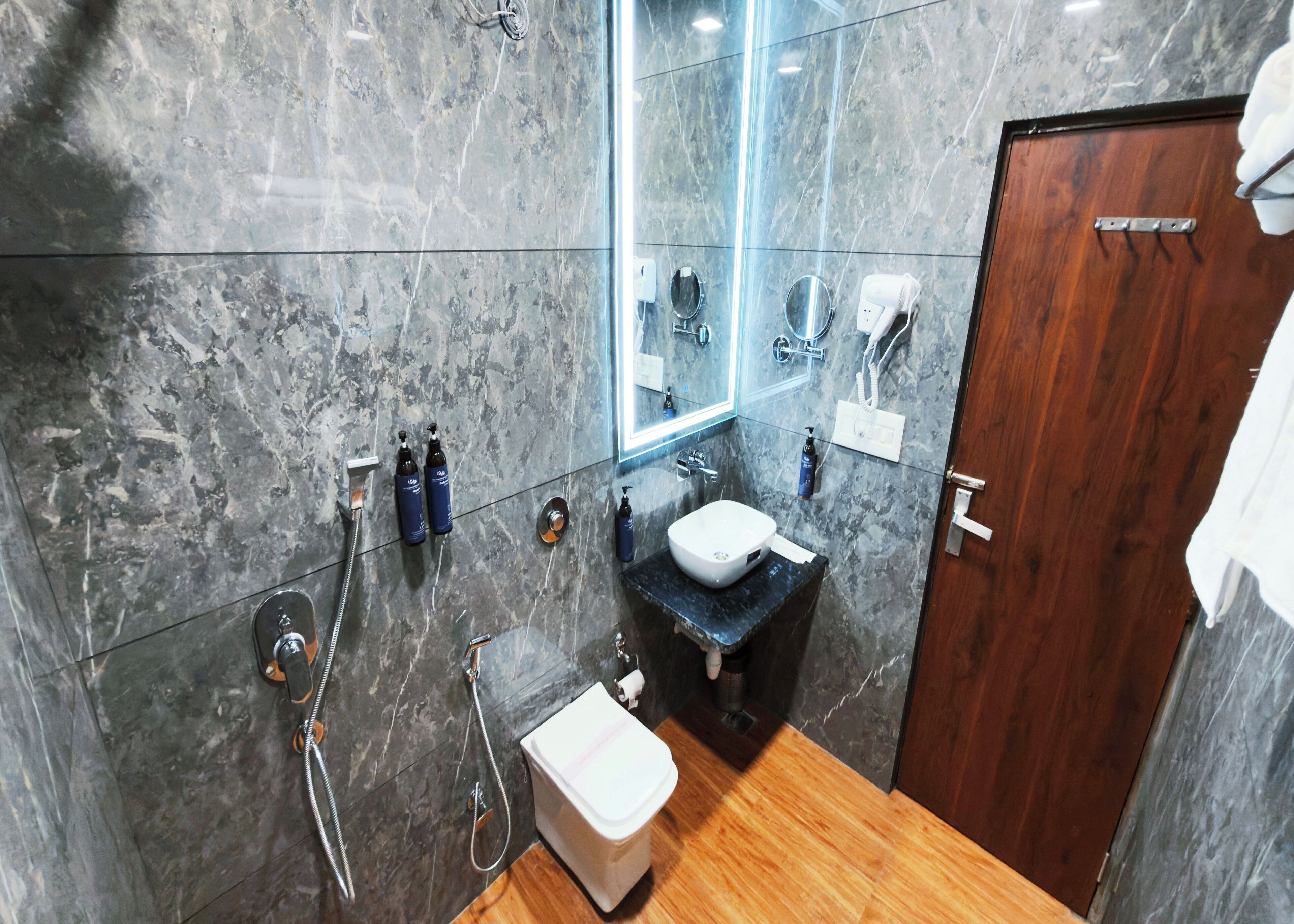 Une salle de bain avec un mur en marbre, un plancher en bois, un lavabo blanc et un miroir.