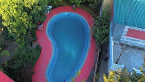 An aerial view of a swimming pool with a red deck, surrounded by trees and a building with a red roof. - The Whispering Oaks Corbett (Ramnagar)