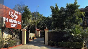 A sign for The Whispering Oaks Corbett, a hotel with a gravel driveway and a red brick wall. - The Whispering Oaks Corbett (Ramnagar)
