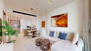 A modern living room with a white sofa, a coffee table, and a dining area with a small island. - Contemporary 1 Bed l City Views l near Circle Mall (Jumeirah Village Circle)