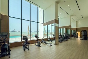 A spacious gym with large windows overlooking a pool and cityscape. - Contemporary 1 Bed l City Views l near Circle Mall (Jumeirah Village Circle)
