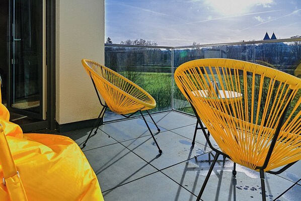A balcony with two yellow chairs and a glass door. - Luxury suite with infrared sauna, electric fireplace & panoramic abbey view (Echternacherbrück)