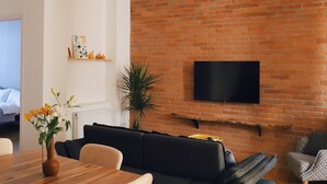 Un salon moderne avec un mur en briques, un téléviseur à écran plat, une table à manger en bois et un canapé noir.