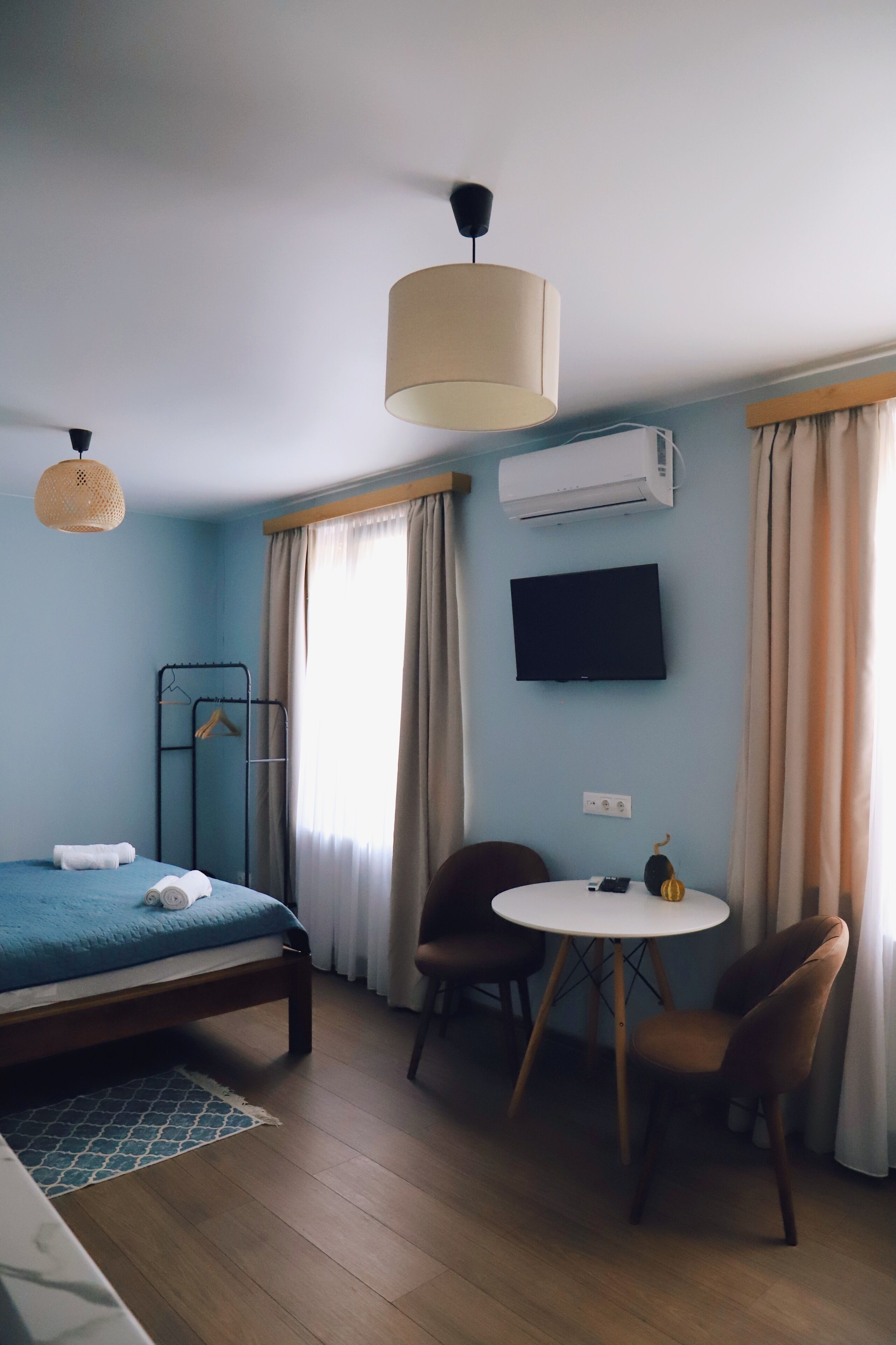 Ein Zimmer mit einem Bett, einem runden Tisch mit zwei Stühlen, einer Pendelleuchte, einer Klimaanlage und einem Fernseher an der Wand.