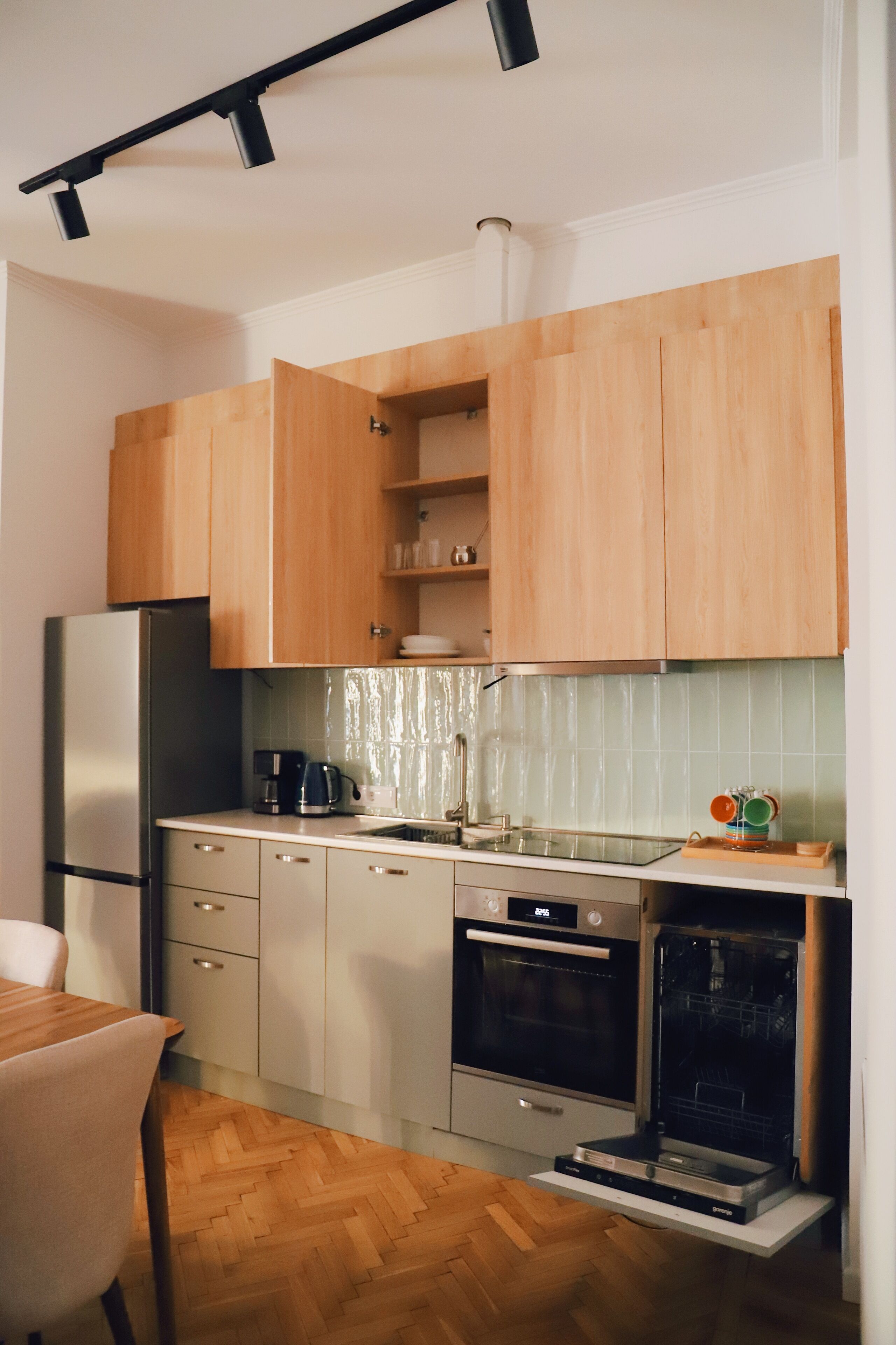 A compact kitchen with wooden cabinets, a stainless steel refrigerator, a dishwasher, and a built-in oven.
