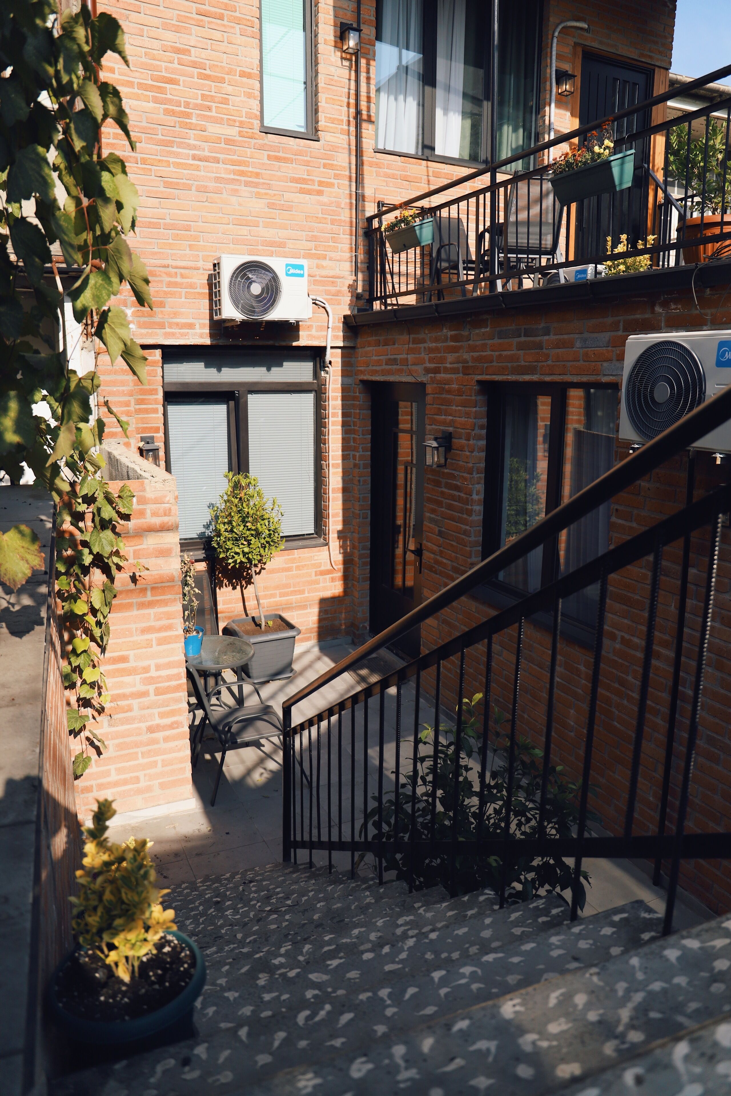 A brick building with two air conditioning units, a small staircase, and potted plants.