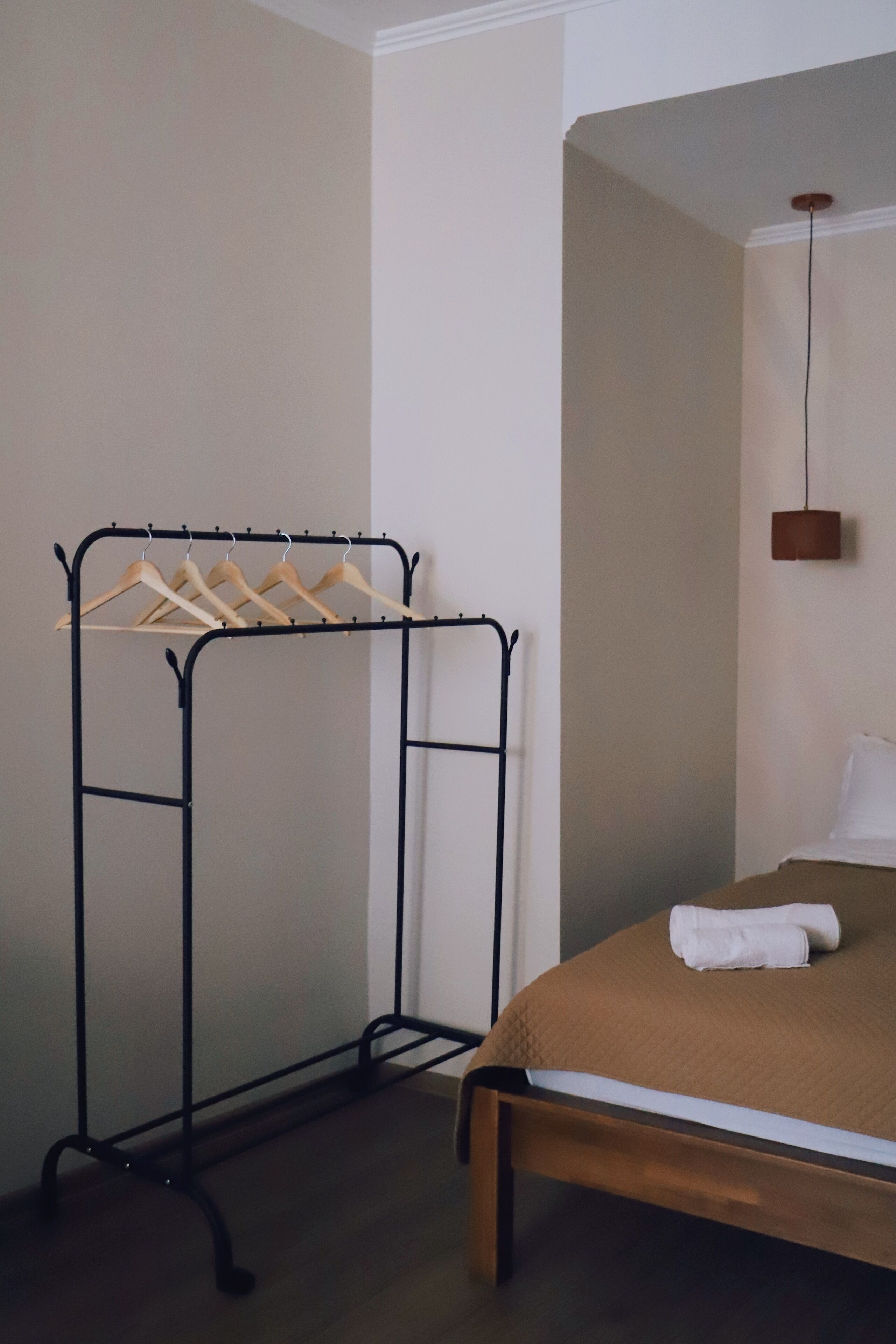 A bedroom with a bed, a wooden hanger rack, and a hanging lamp.